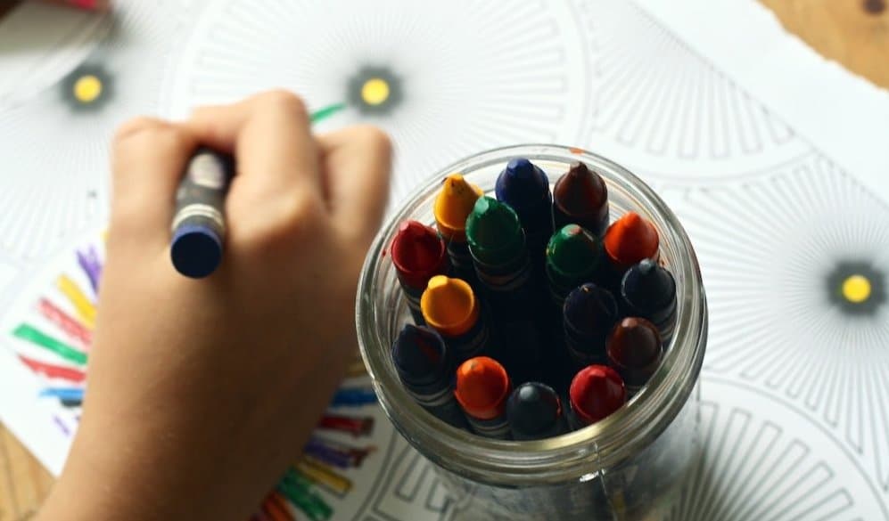 child drawing on paper with crayons